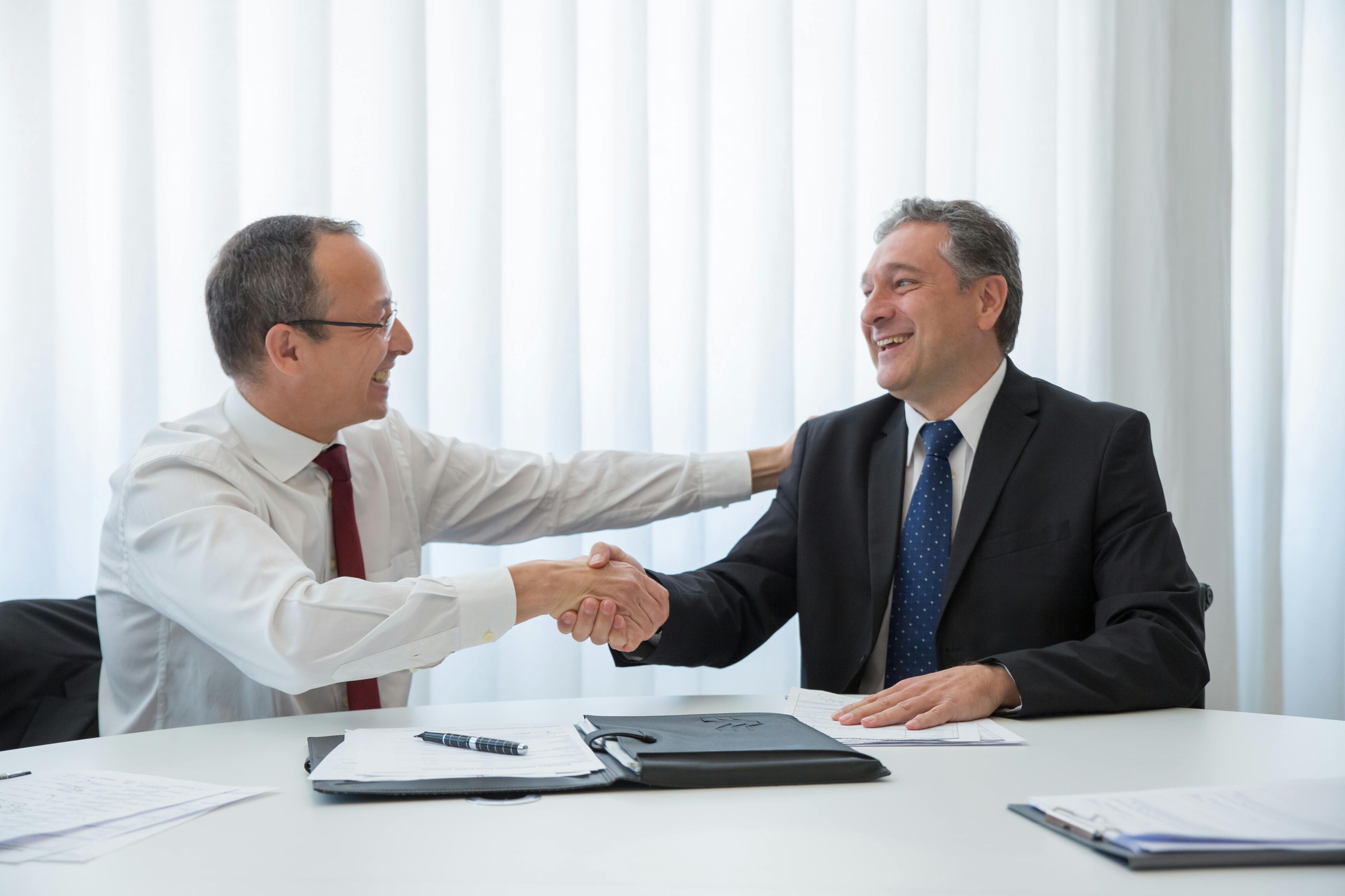 two businessmen shaking hands and smiling in office